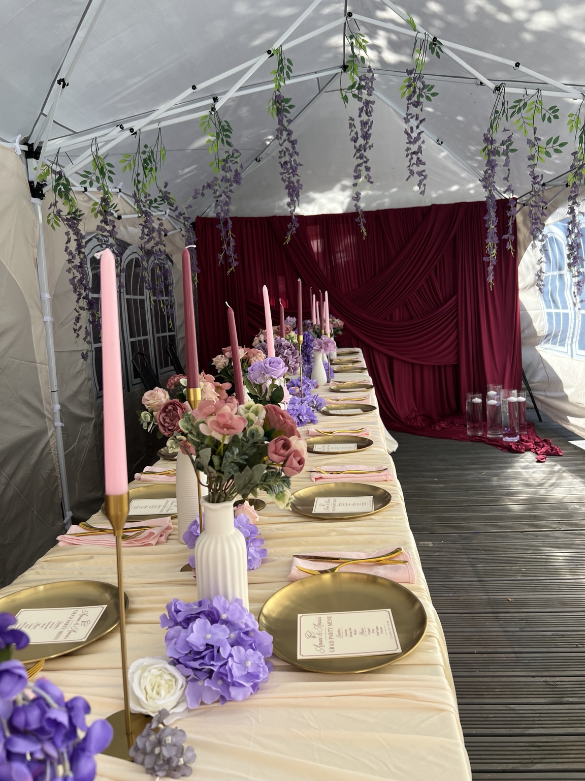 Burgundy draped backdrop with pink candles, colourful flowers and gold table settings by Nour Occasions