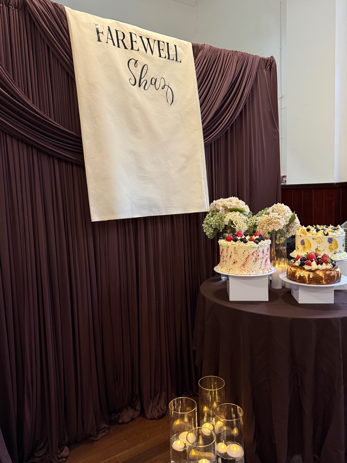 Chocolate brown draping with a personalised farewell banner, cake display and candles by Nour Occasions