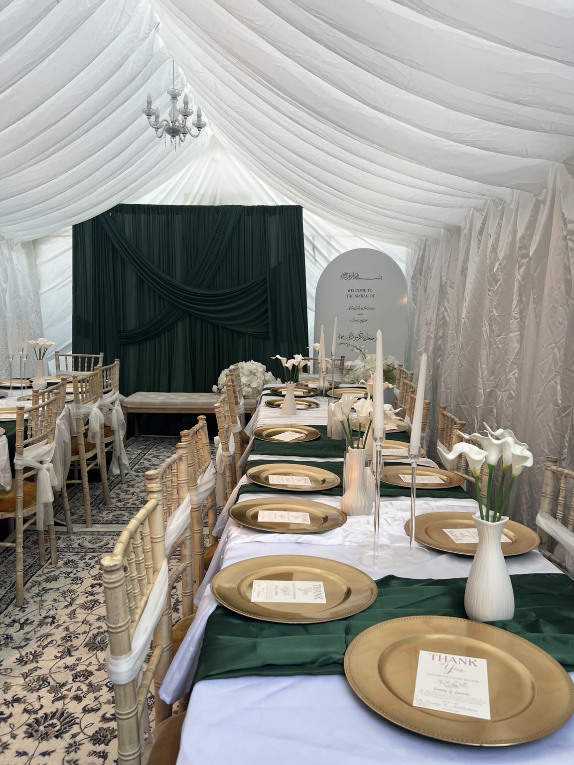 Green nikah backdrop, welcome board and tables with gold plates and white flowers by Nour Occasions