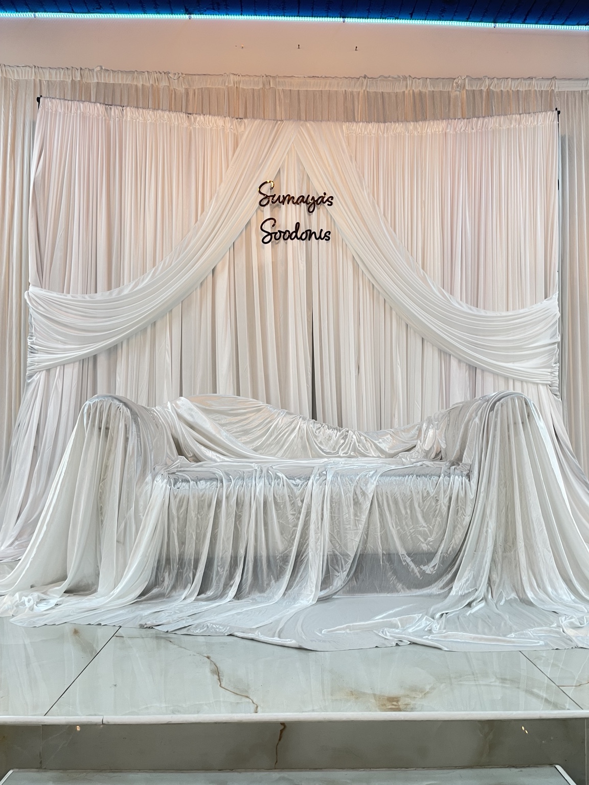 White draped backdrop and fabric-covered bench with personalised lettering by Nour Occasions